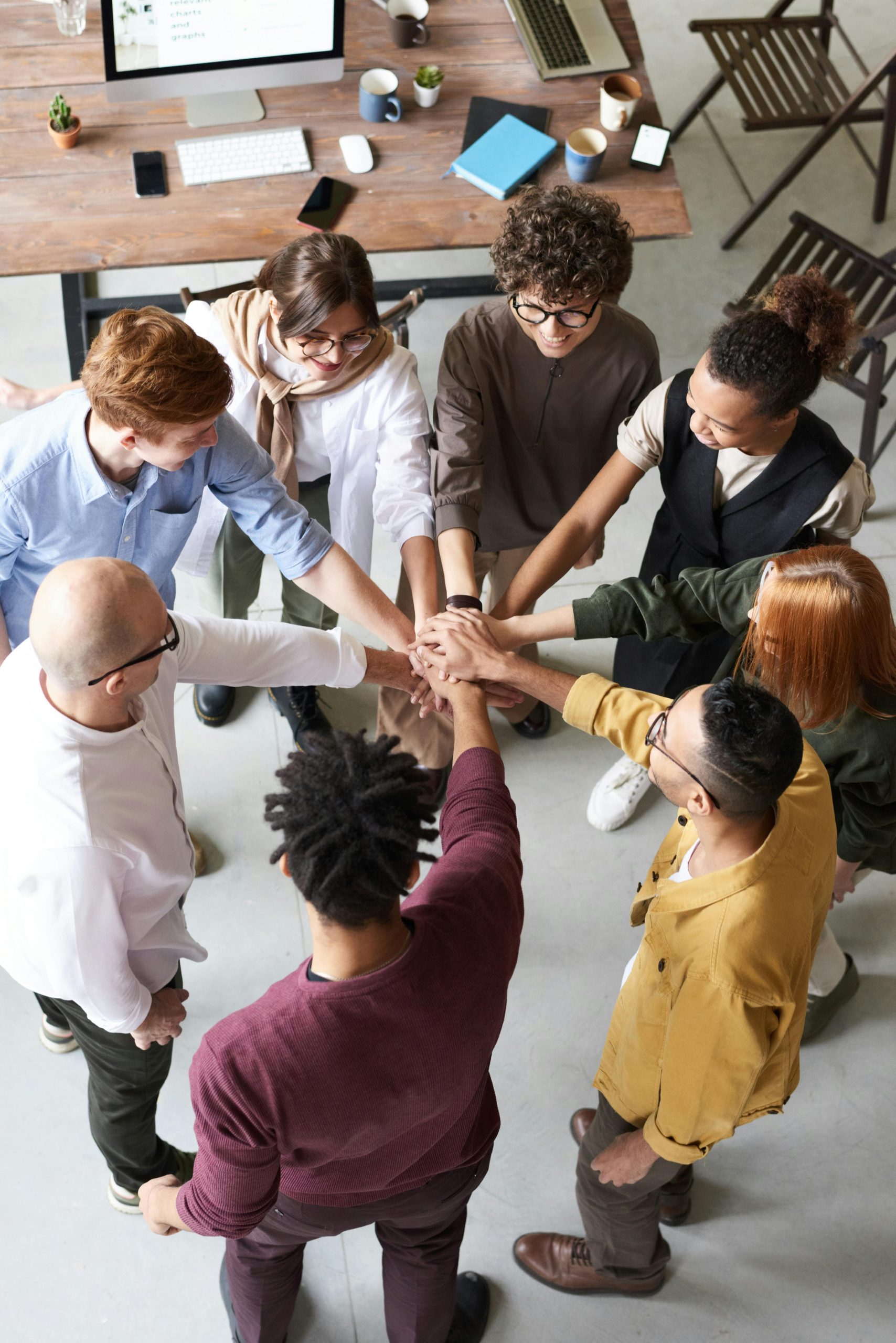 About diverse group of professionals joins hands in a team-building exercise indoors.